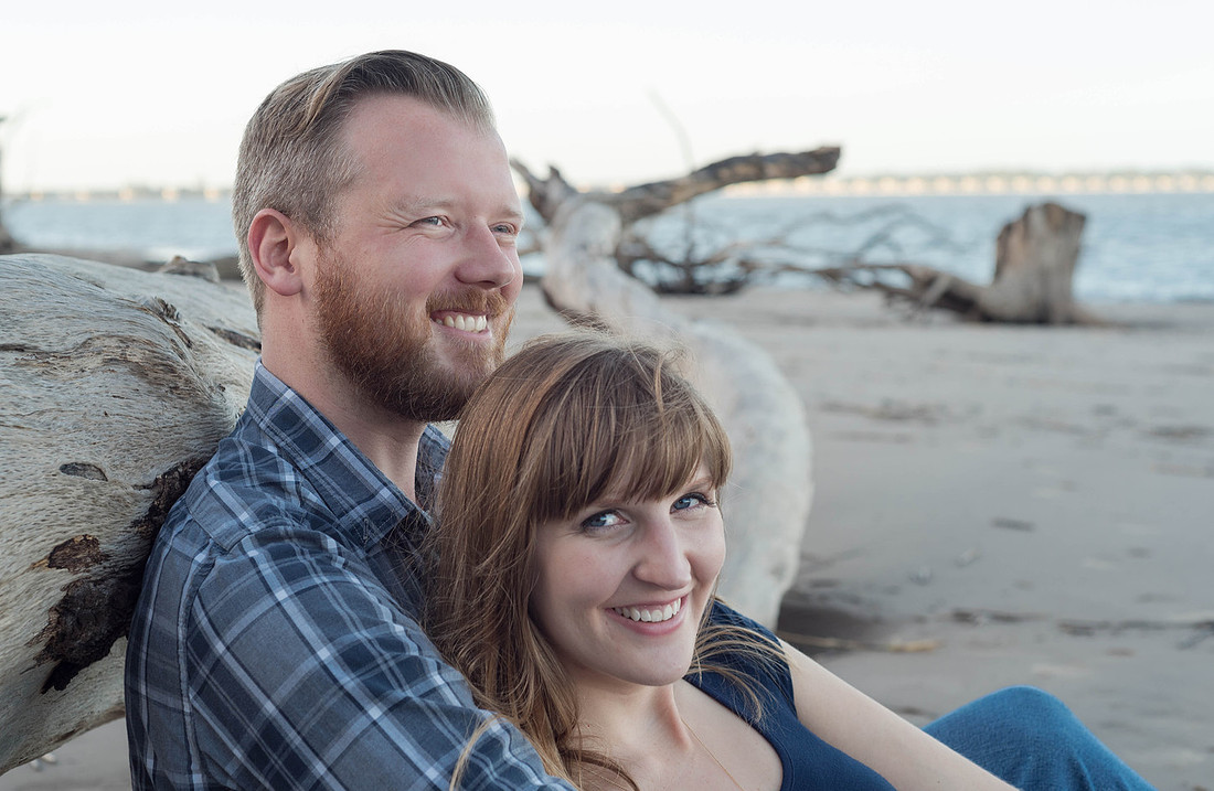 the couple sitting against a horizontal piece of drift wood on the beach in Big Talbot Island for their Engagement Session